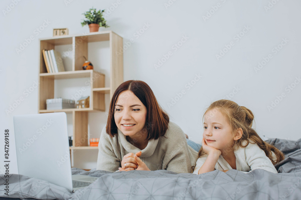 Mom and daughter watching video on laptop while lying in bed Mom and daughter watching video on laptop while lying in bed
