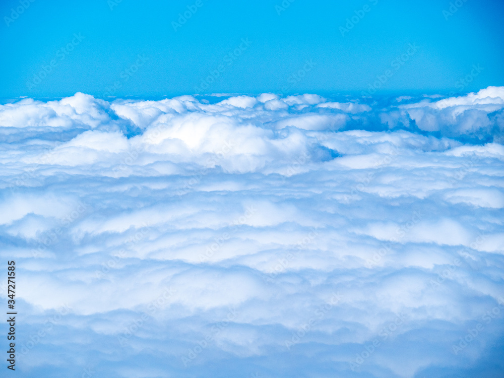 Above the fluffy blue/white clouds with a bright blue sky and copy space.