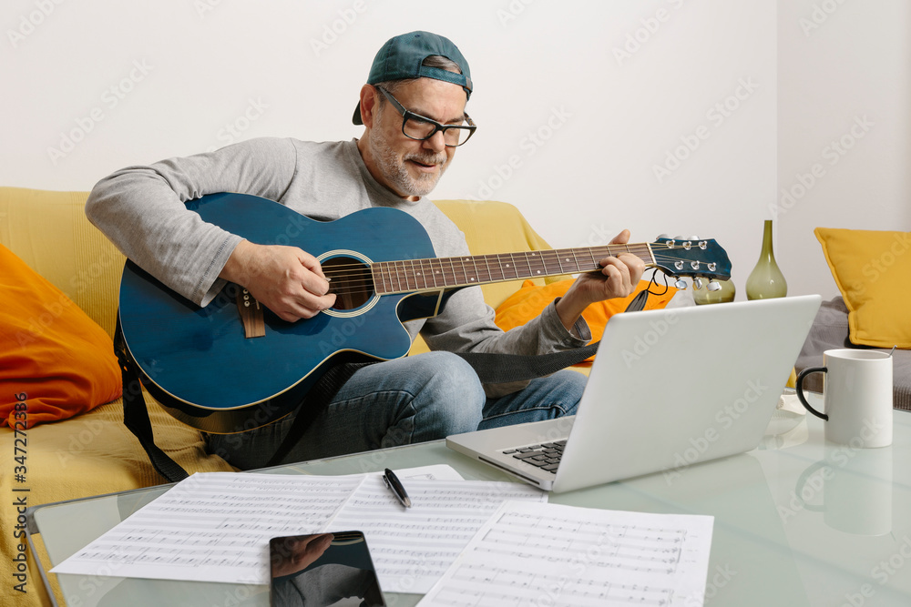 Musician playing the guitar and composing music with his colleagues by video conference through his laptop Musician playing the guitar and composing music with his colleagues by video conference through his laptop