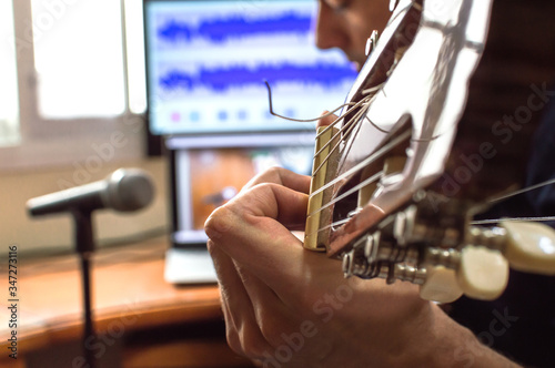 Person playing guitar and recording the audio using microphone and technology at home. Amateur musician recording music.