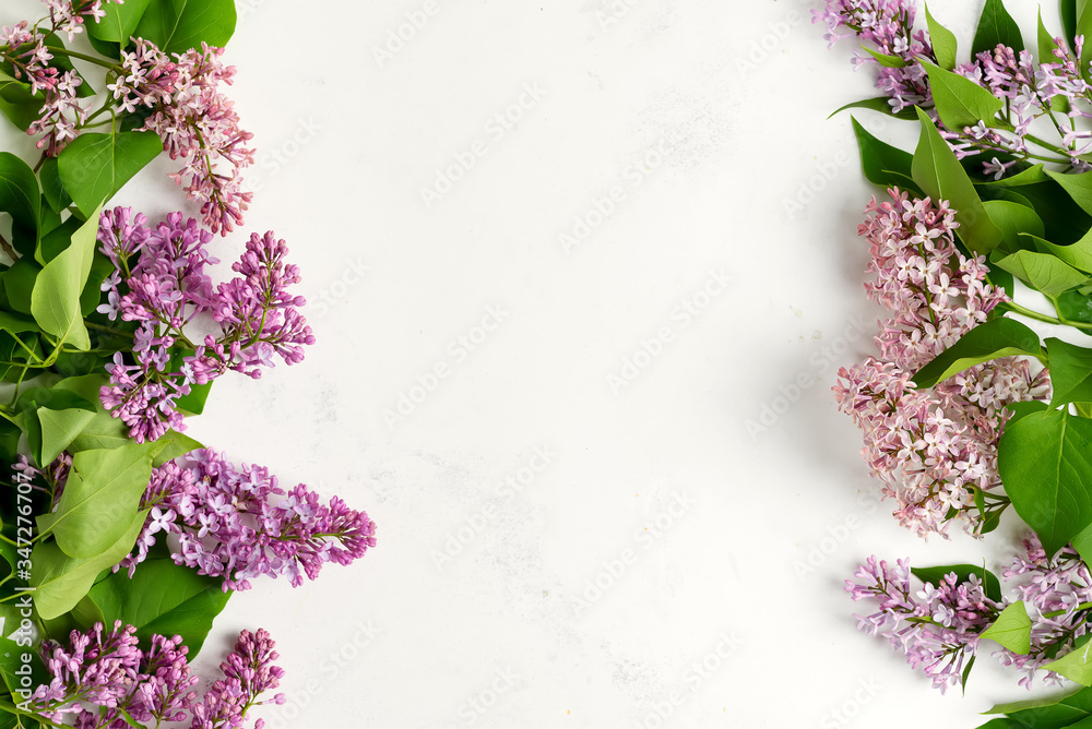 Greeting frame from fresh lilac flowers with green leaves on a light grey marble background. Top view.