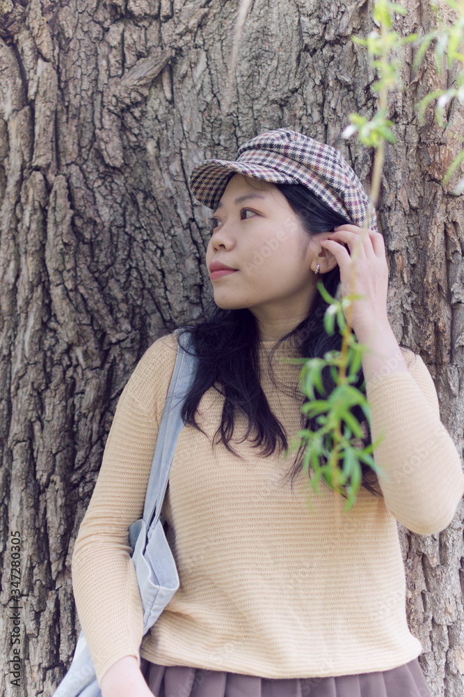 Attractive Asian Female College Student Looking Into The Distance While Leaning Against A Tree