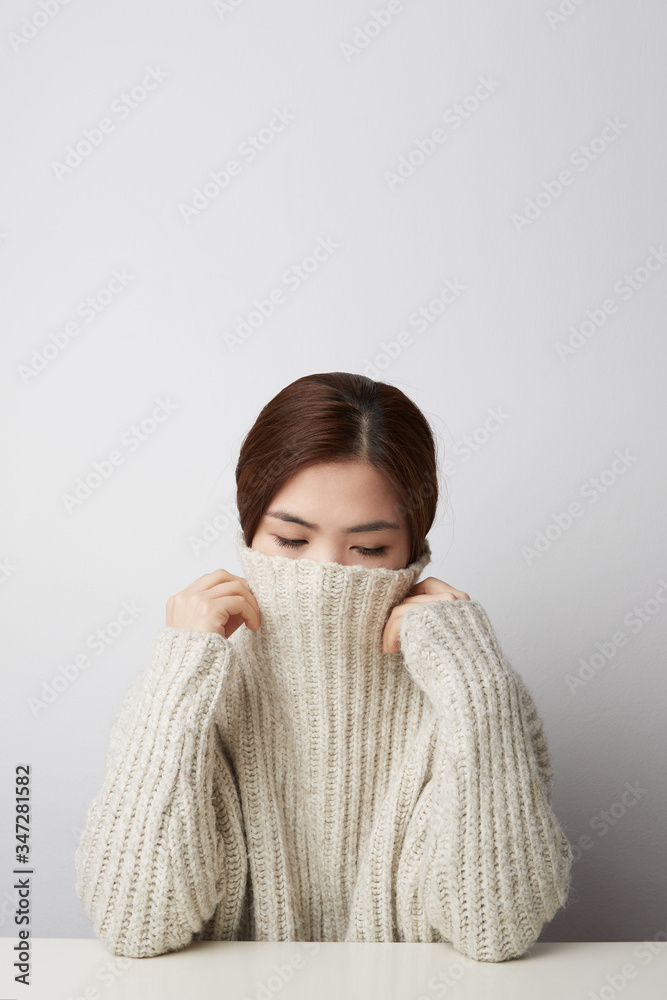 Studio shot of happy asian woman wears beige knitted jumper, holds hands under chin. Vertical shot. Isolated. Studio shot of happy asian woman wears beige knitted jumper, holds hands under chin. Vertical shot. Isolated.