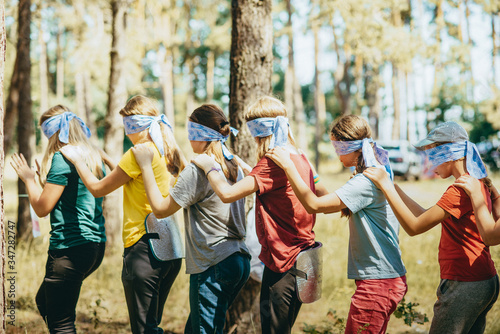 The teenagers stand next to each other and put their hands on the shoulders of a person standing nearby. Eyes blindfolded at all. Team building exercise, team spirit. Strengthening team relationships.