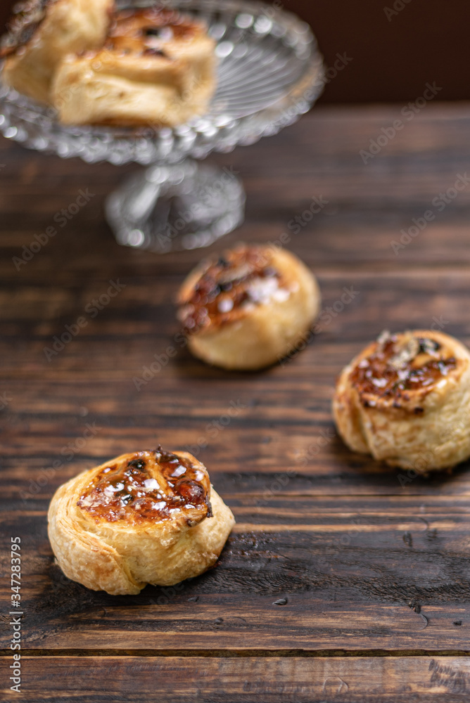 Homemade glazed puff pastry cinnamon rolls with custard and raisins on wooden background.