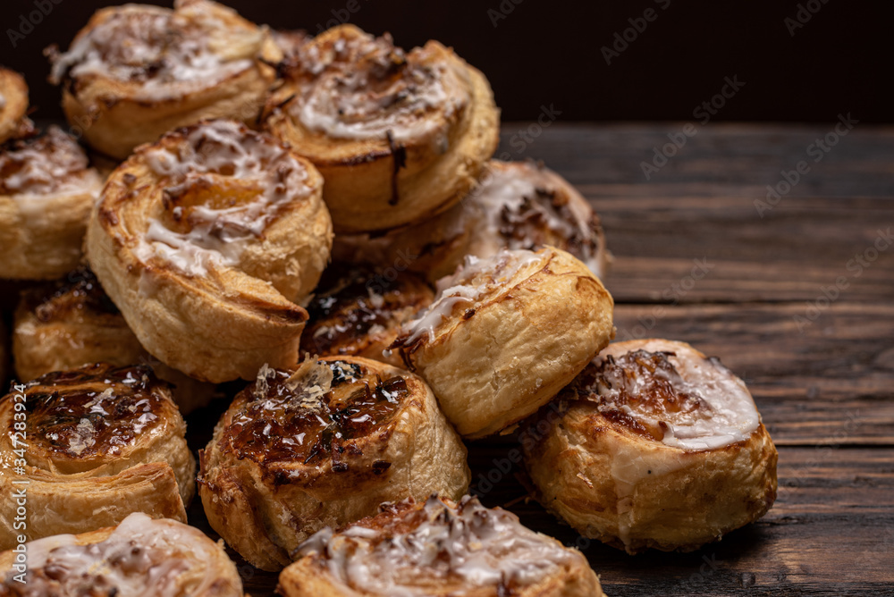 Homemade glazed puff pastry cinnamon rolls with custard and raisins on wooden background.