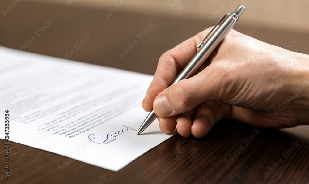 A businessman sits at an office Desk and signs a contract with a ballpoint pen A businessman sits at an office Desk and signs a contract with a ballpoint pen