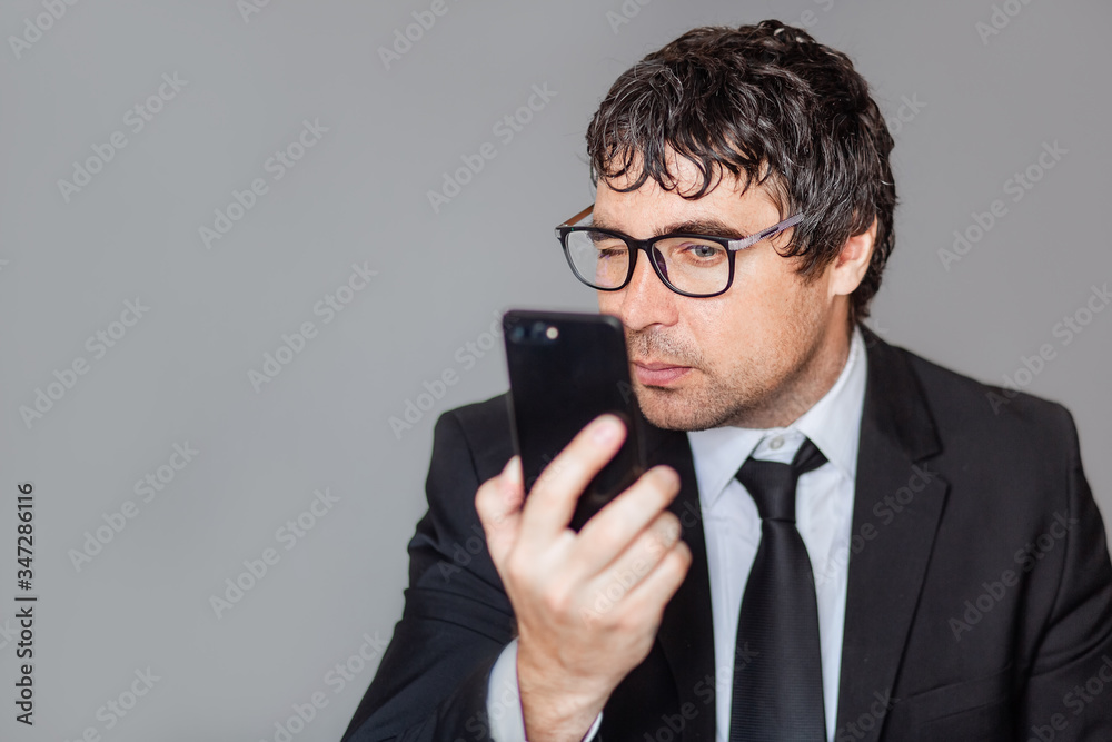 A male businessman in a black suit and glasses is talking on the phone. Grey isolated background. A male businessman in a black suit and glasses is talking on the phone. Grey isolated background.
