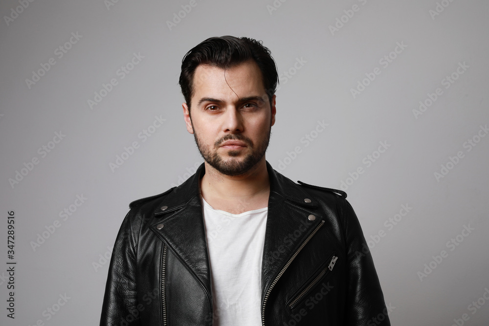 Horizontal shot of modern stylish young hipster man in a leather biker jacket posing over a white background. Isolated.