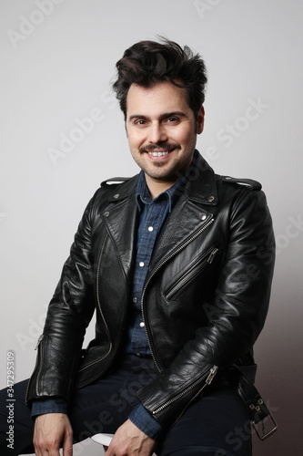 Vertical shot of modern stylish young hipster man with happy face in a leather jacket posing over a white background.