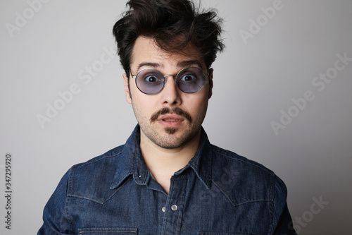 Bearded man in the denim outfit with bright white t-shirt wearing stylish spectacles posing over white wall. Isolated.