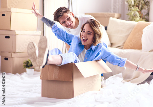 Happy couple having fun and riding in cardboard boxes at new home