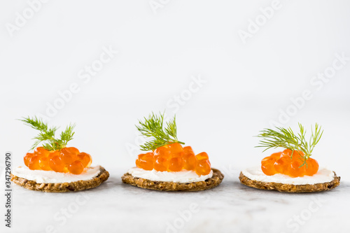 A close up view of a row of cracker and cream cheese canapes topped with red caviar and garnished with dill.