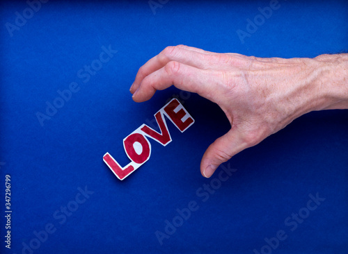 Une main d'homme va saisir un texte imprimé love, amour en rouge, sur fond bleu