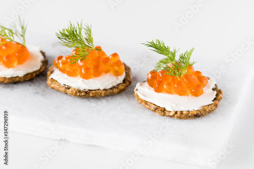A close up of three cracker and cream cheese canapes topped with red caviar and garnished with dill ready for eating.