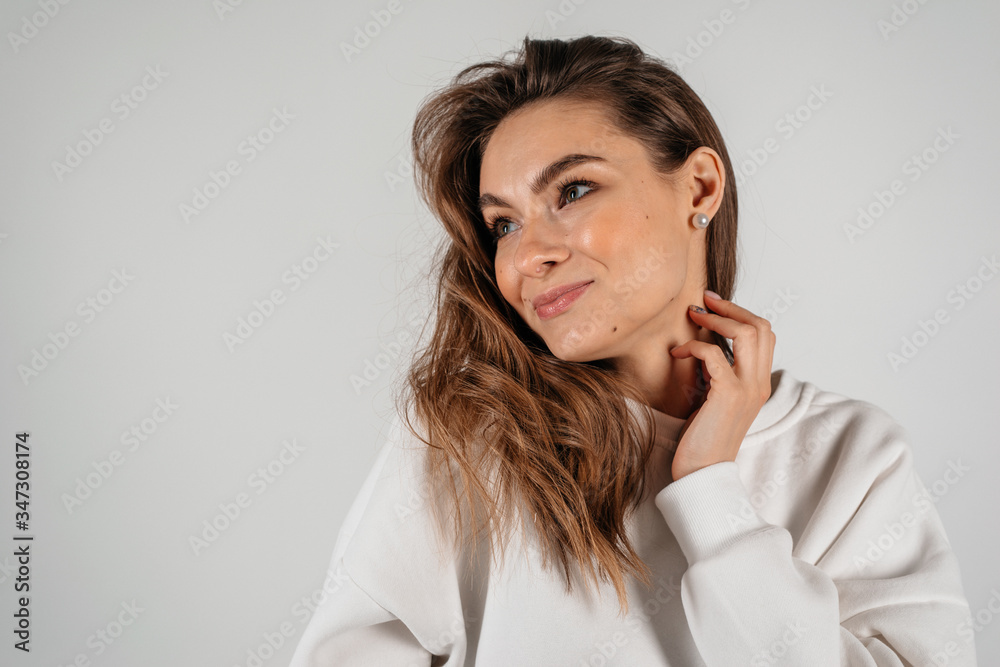 Beautiful young woman posing at studio, looking to the side smiling, on white background Beautiful young woman posing at studio, looking to the side smiling, on white background
