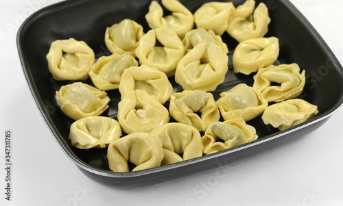 Italian traditional tortellini pasta or ravioli stuffed with spinach in the pan, isolated.