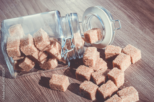 Brown cane refined sugar in a jar on a wooden background.