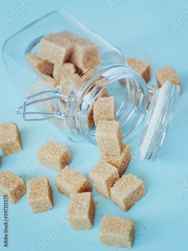 Brown cane refined sugar in a jar on blue background.