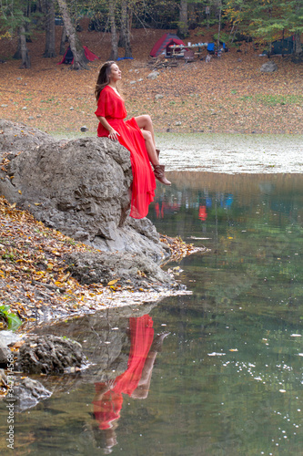 woman in the autumn forest. fairy-tale reflection in the lake. Fashionable woman standing over lake in park. beautiful young woman. Beauty girl with a red long dress near the lake. Fashion photo, copy