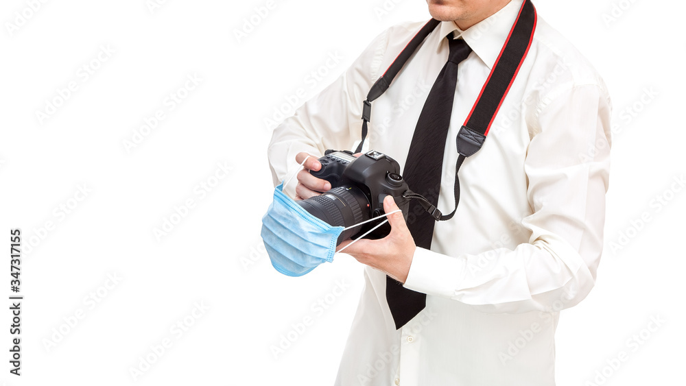 photographer in shirt with tie holds dslr camera with medical protective mask on the lens, concept work photojournalist during quarantine pandemic virus isolated on white background with copy space. photographer in shirt with tie holds dslr camera with medical protective mask on the lens, concept work photojournalist during quarantine pandemic virus isolated on white background with copy space.