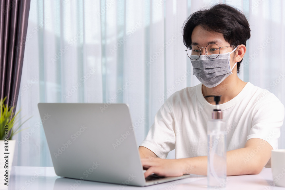 Asian business young handsome man glasses, wearing protective mask with disinfectant gel beside he work from home office remote online with laptop computer quarantines disease coronavirus or COVID-19 Asian business young handsome man glasses, wearing protective mask with disinfectant gel beside he work from home office remote online with laptop computer quarantines disease coronavirus or COVID-19