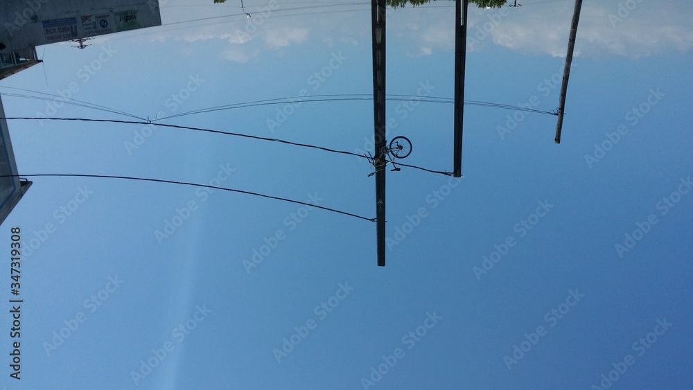 Low Angle View Of Bike In Power Lines Against Blue Sky - obrazy, fototapety, plakaty 
