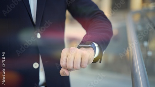 Close up of man dressed in business suit white shirt and blue jacket using smartwatch on his left hand. On background of blurred floor in shopping center