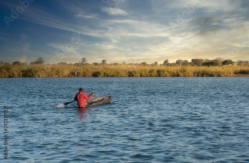 One young African adult wearing a bright red shirt in a handmade wooden boat on the Kavango River in Namibia, Africa