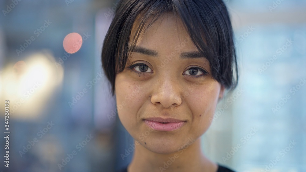 Obraz premium Close up portrait shot of smiling happy black hair asian female with beautiful smile wearing grey sweatshirt standing on background of big mall center. Blue background