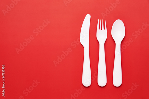 Plasic white cutlery set with red background. Top view