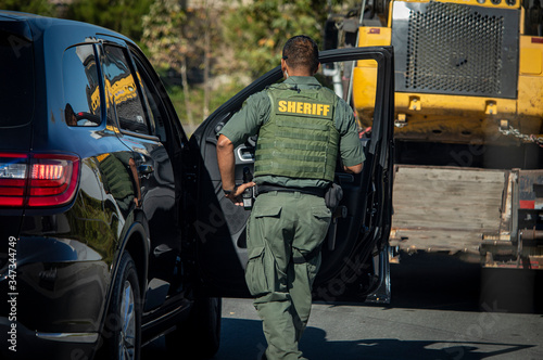 Behind view of police officer in bullut proof vest looking into passanger side of car at the scene of an accident photo