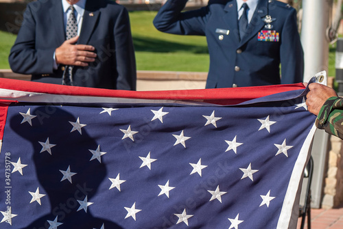 United States Air Forece Officer and civilian honorng a flag being folded at a ceremony to honor MIA/POW.  Shadow of soldier is on the flag