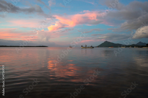 Fishermen go on a boat for evening fishing on the background of a colorful sunset. Mauritius, Indian Ocean