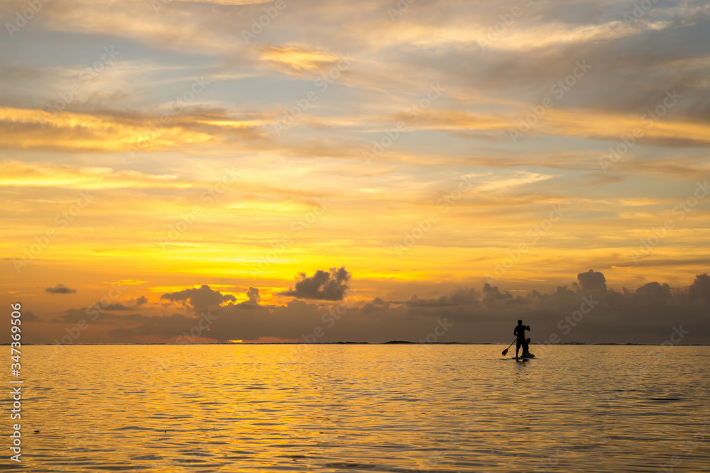 pair of lovers coming back from the ocean by paddle board  against the backdrop of a beautiful sunset in Mauritius