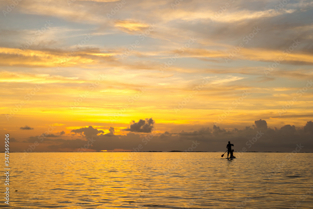 pair of lovers coming back from the ocean by paddle board against the backdrop of a beautiful sunset in Mauritius pair of lovers coming back from the ocean by paddle board against the backdrop of a beautiful sunset in Mauritius