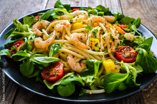 Spaghetti with prawns and vegetables on wooden background