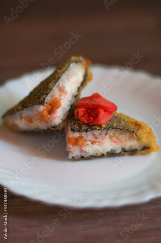 Fried sushi on a white plate with cream cheese, salmon, and ginger on wooden background. Side view. Japanese food.