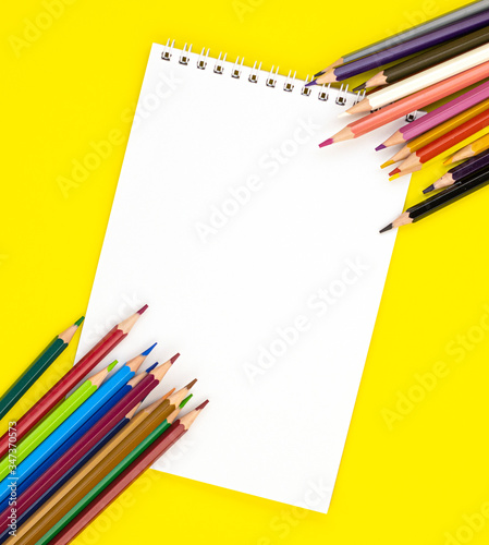 white blank Notepad in the center and colored pencils in the corners, isolated on a yellow background. stationery for school preparation. background for designers with space for text. online learning