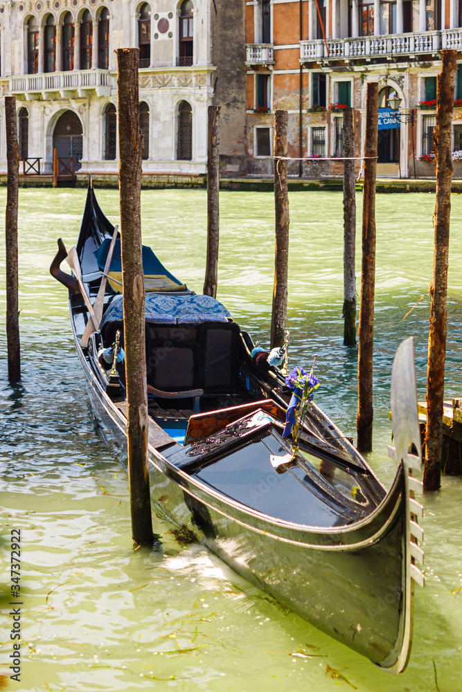 Venetian gondola at the pier between the wooden poles on the Grand Canal on a sunny summer day, Venice, Italy
