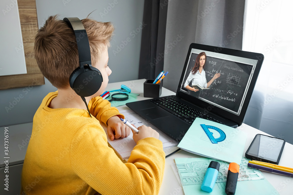 Distance learning, a boy in headphones sits at a table at home looking in a beech laptop. The concept of online education, home education, technology, school. Distance learning, a boy in headphones sits at a table at home looking in a beech laptop. The concept of online education, home education, technology, school.