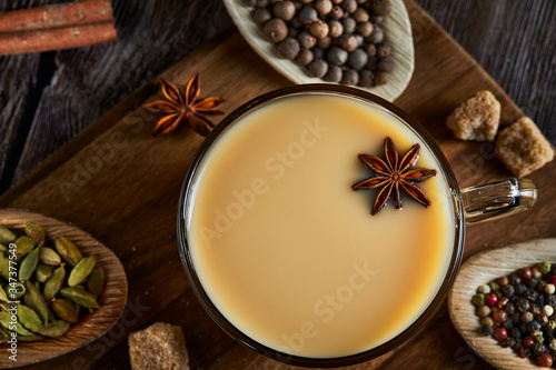 Traditional Indian drink - masala tea with spices. Cinnamon, cardamom, anise, sugar, cloves, pepper on a dark wooden background. © AlexanderD