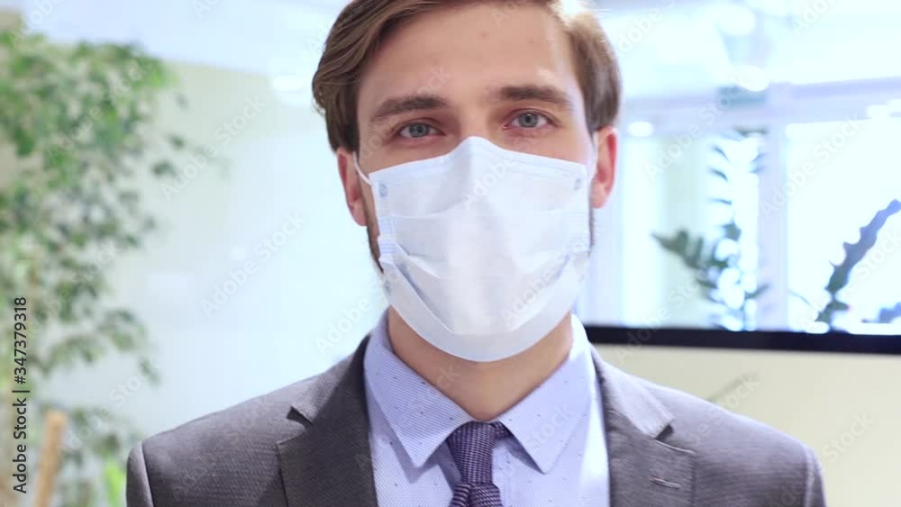 Serious businessman protective turquoise medical mask on face, head to the side, looking at the camera.