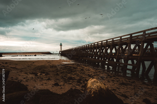 pier on the beach leading to a lighthouse