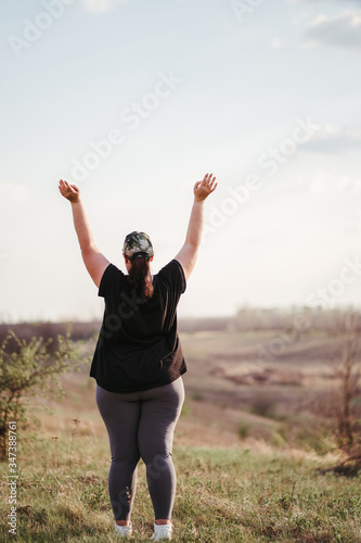 Body positive, success, freedom, happiness, confidence, self esteem. Overweight woman rising hands to the sky. Obesity and outdoor activity