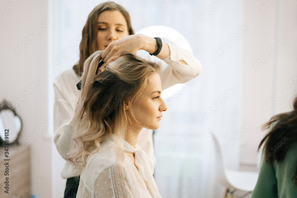 Two make-up artistes applies hair and makeup to the bride in dressing room. Concept of backstage work. Two make-up artistes applies hair and makeup to the bride in dressing room. Concept of backstage work.