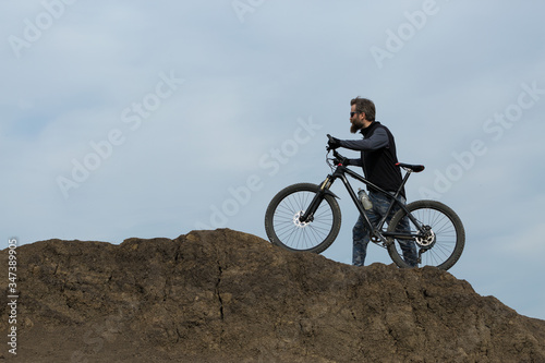 Sports brutal bearded guy on a modern mountain bike. Beautiful view from the mountain. Panoramic view for banner.