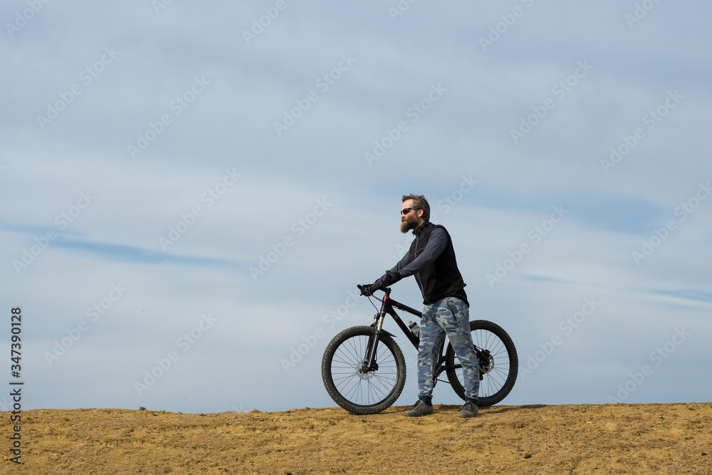 Sports brutal bearded guy on a modern mountain bike. Beautiful view from the mountain. Panoramic view for banner.
