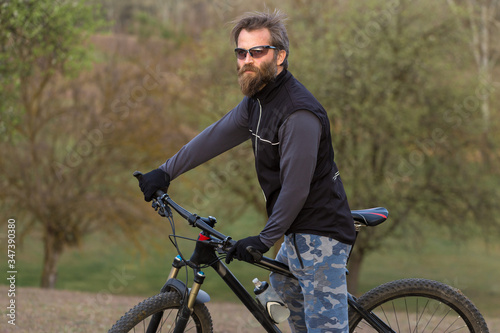 Fototapeta Naklejka Na Ścianę i Meble -  Sports brutal bearded guy on a modern mountain bike. Cyclist on the green hills in the spring.