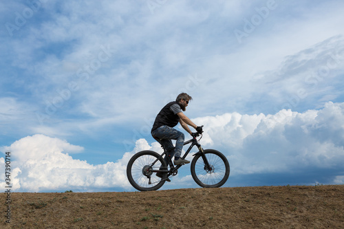 Sports brutal bearded guy on a modern mountain bike. A cyclist in a salt deserted place by the lake.